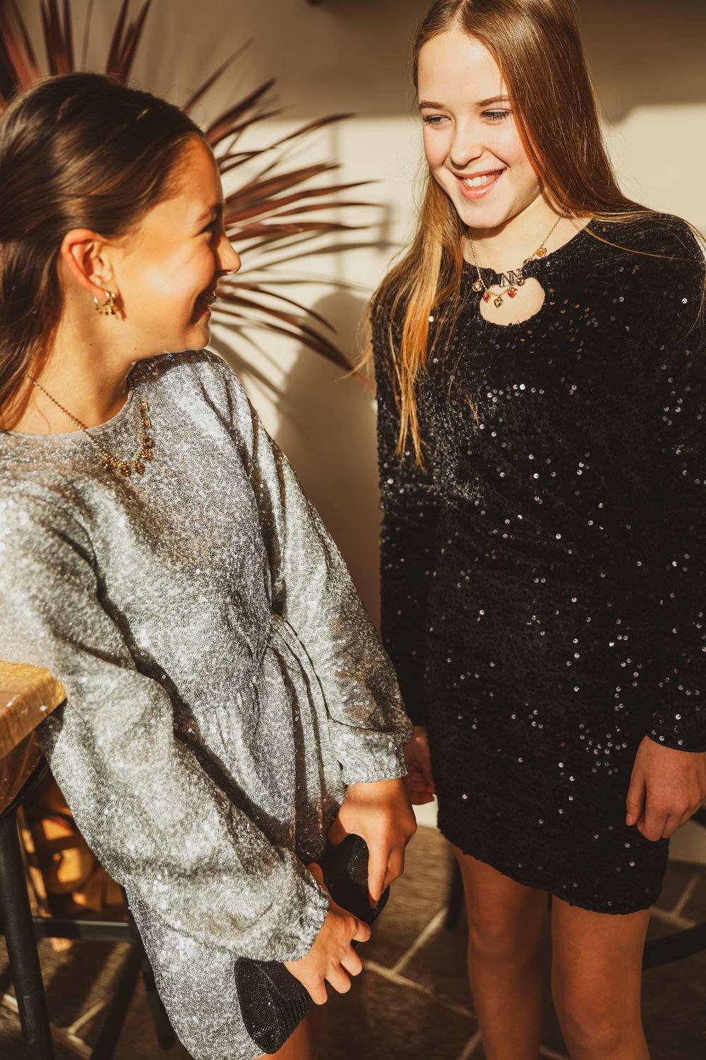 Two friends in sparkly dresses sharing a laugh at a party.