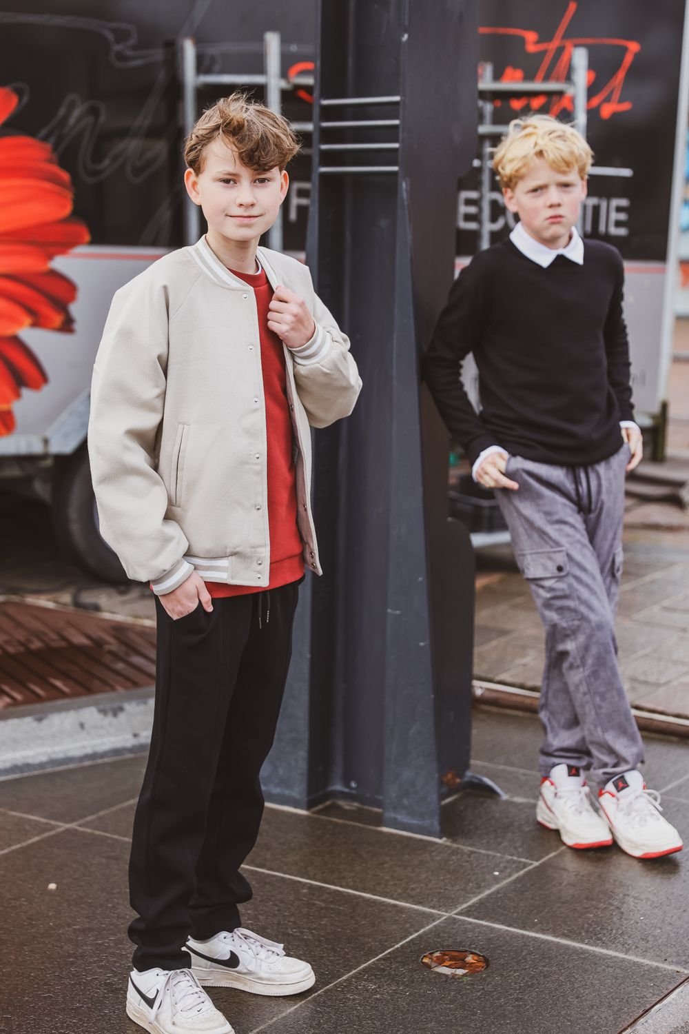 Two young models in casual winter outfits posing near a storefront.