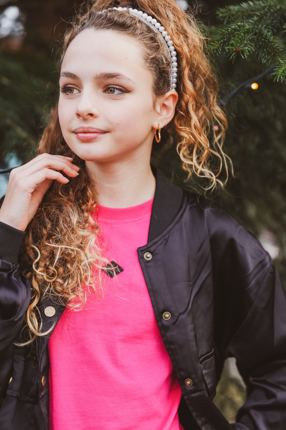 Portrait of person with curly hair wearing pearl headband and pink shirt.