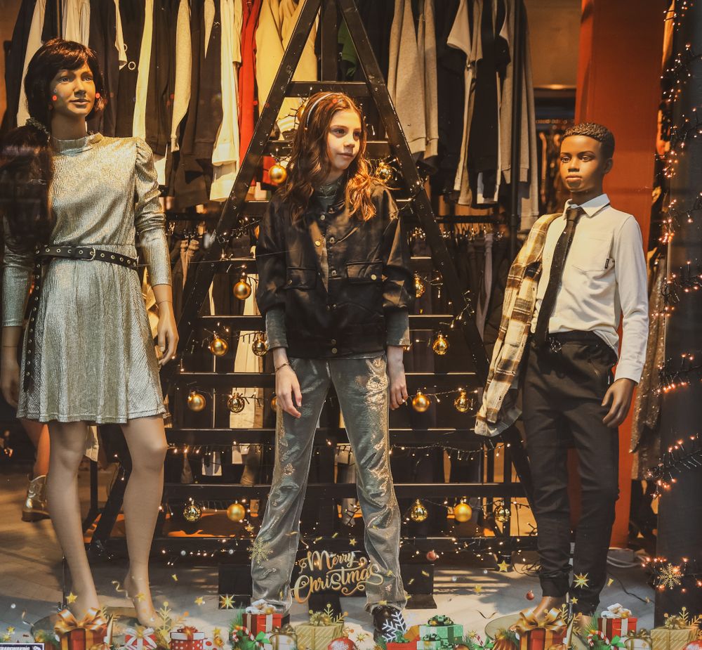 Three models pose in front of a vintage clothing display with stylish retro outfits.