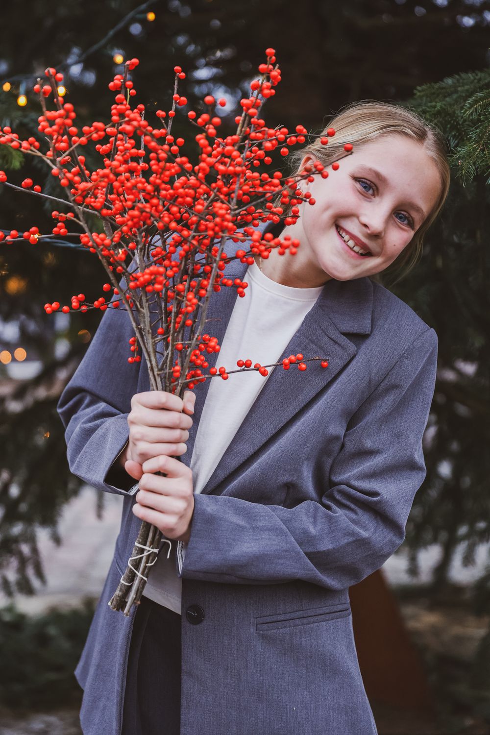 Young person in blazer holding red winter berries against dark background.
