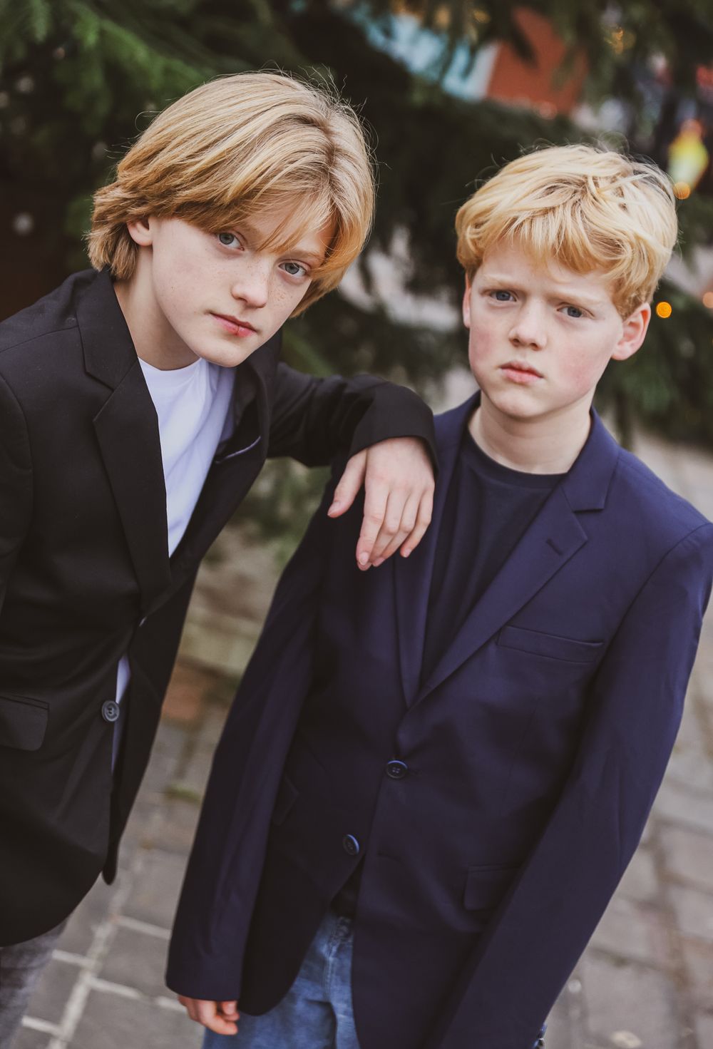 Two young models in stylish blazers posing together outdoors.