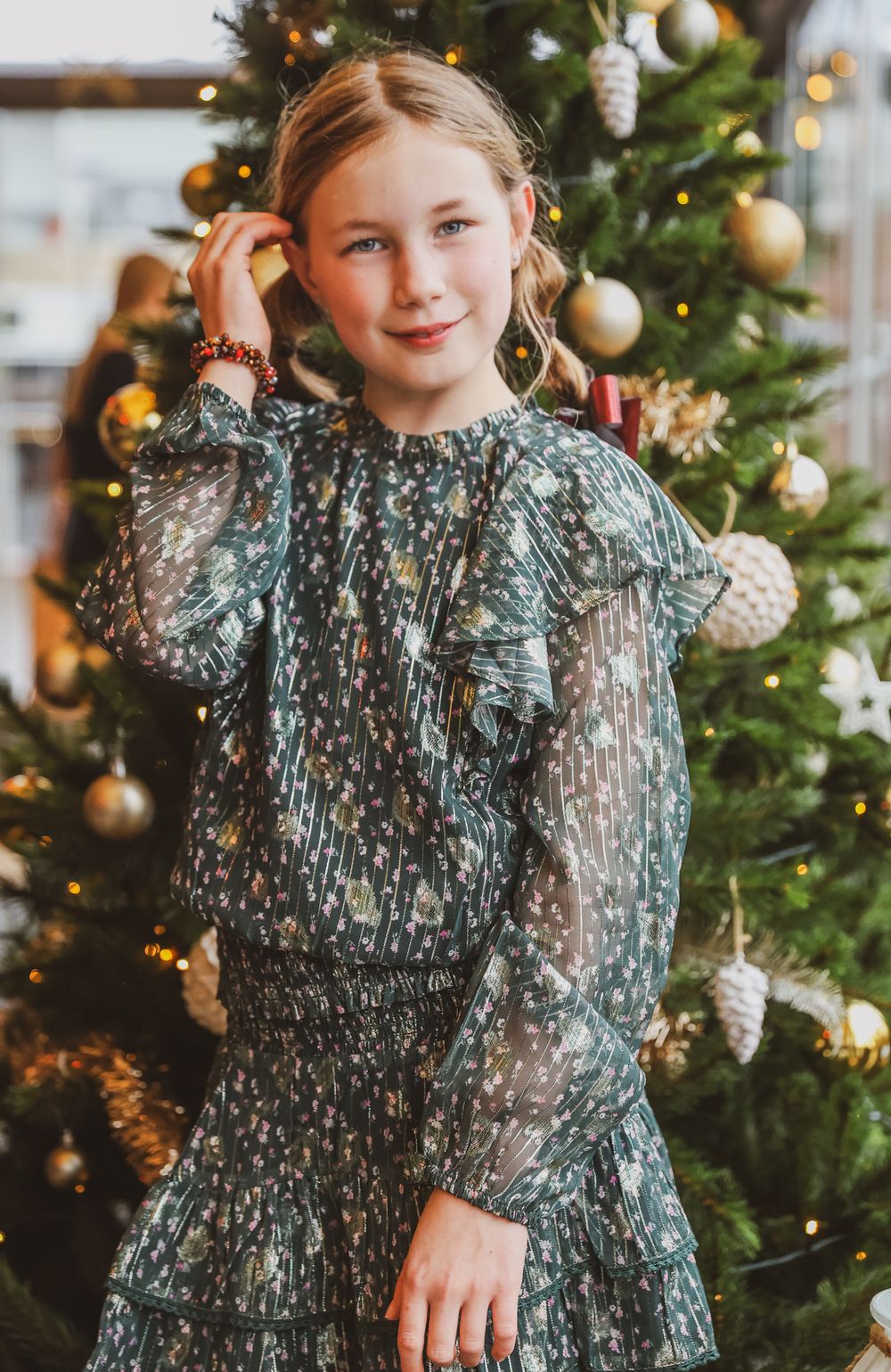 Young person wearing elegant green dress posing next to decorated Christmas tree.