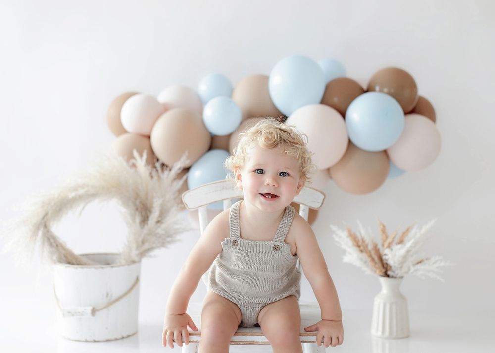 Neutral toned birthday setup with brown and blue balloon arch and pampas grass decorations.