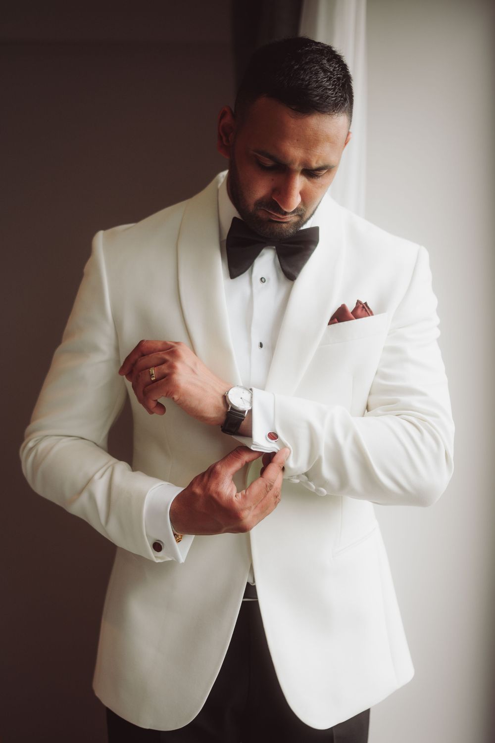 Man in white tuxedo jacket adjusts his cufflinks while getting ready.