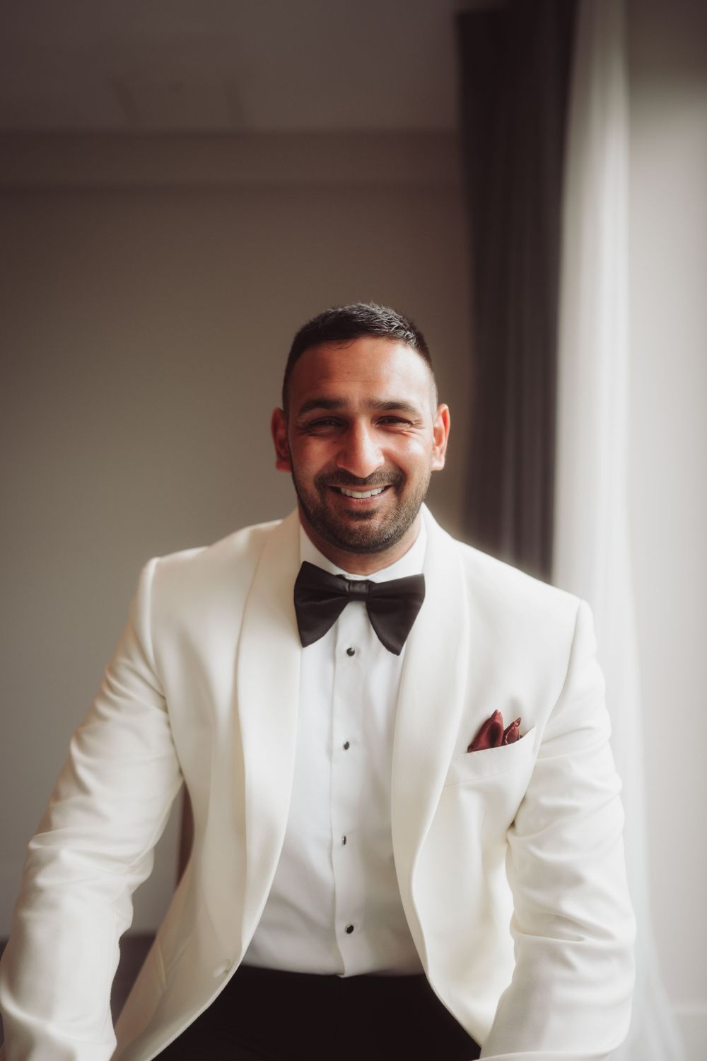 A person in a crisp white tuxedo jacket and black bow tie smiles warmly at the camera.