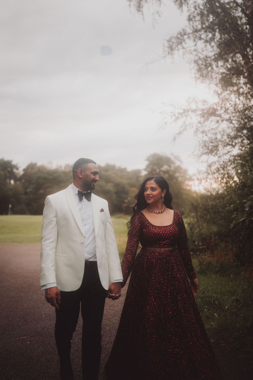 Couple in formal attire walks hand in hand along outdoor path.