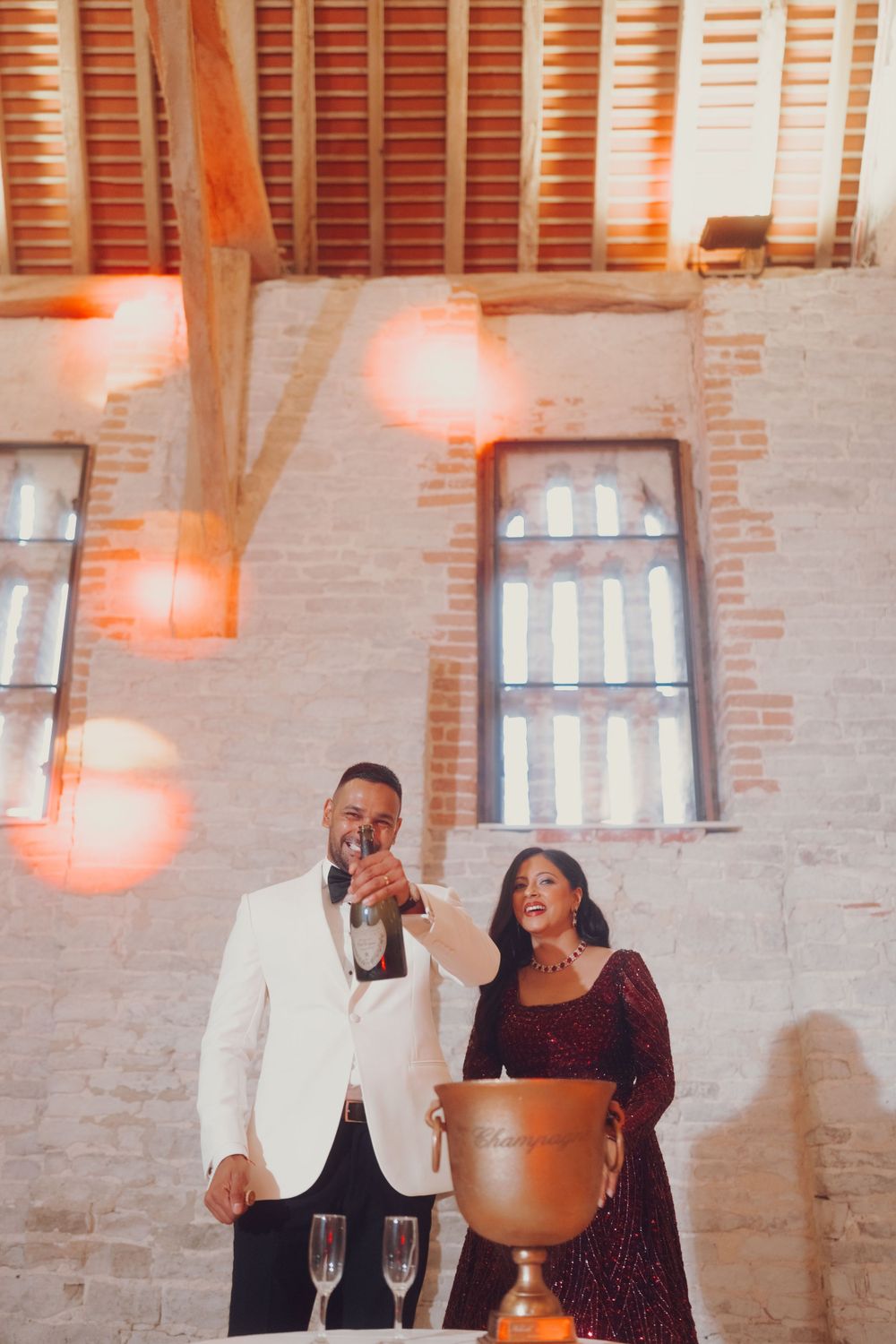 Elegant couple posing in industrial venue with warm lighting and brick walls.