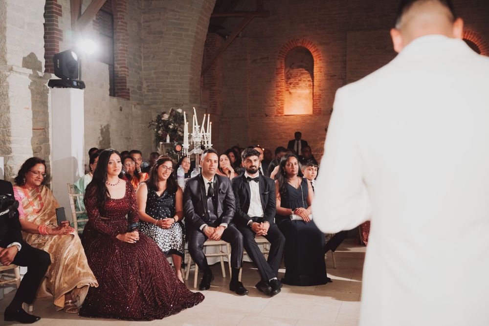 Wedding guests seated in rows watch attentively during an indoor ceremony.