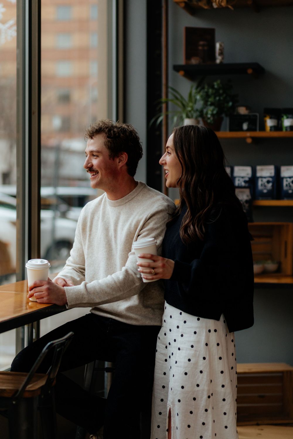 A joyful couple shares coffee and laughter by a cafe window while enjoying a cozy cafe atmosphere.