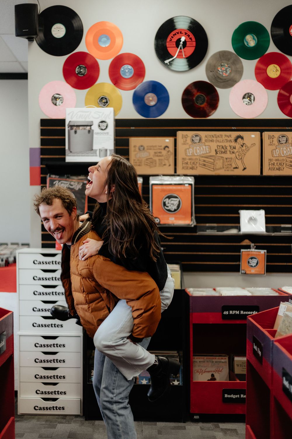 A joyful candid moment captured in a record store with vinyl records displayed on the wall and cassette boxes stacked nearby.