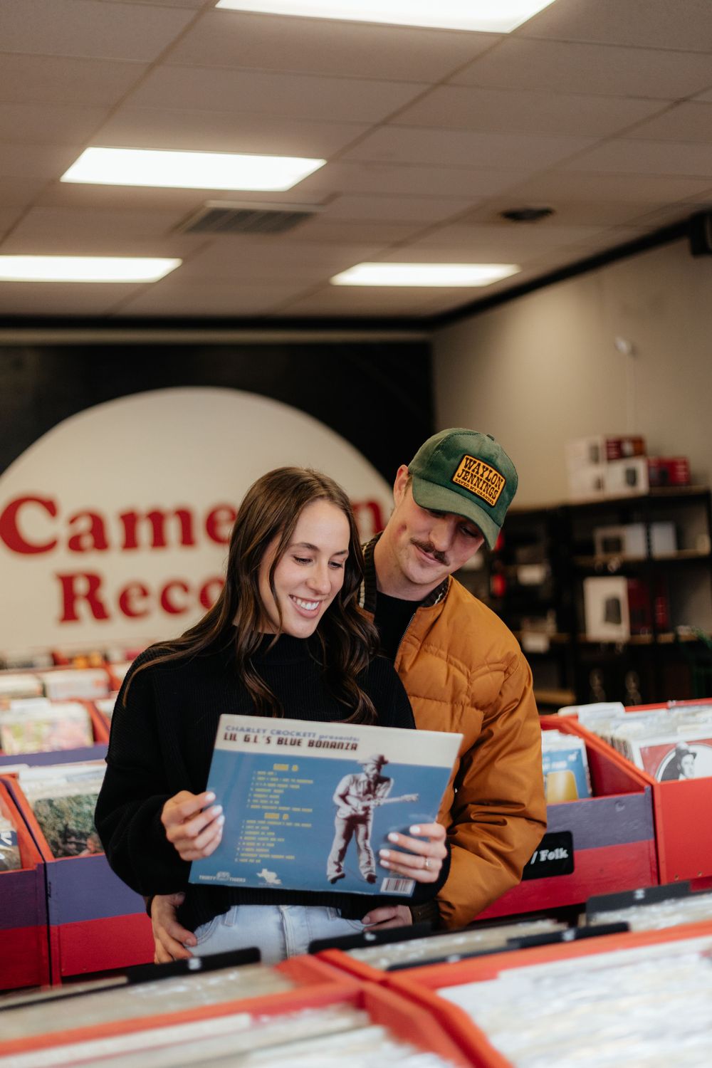 A couple browses through vinyl records together at a music store with red signage and fluorescent lighting.