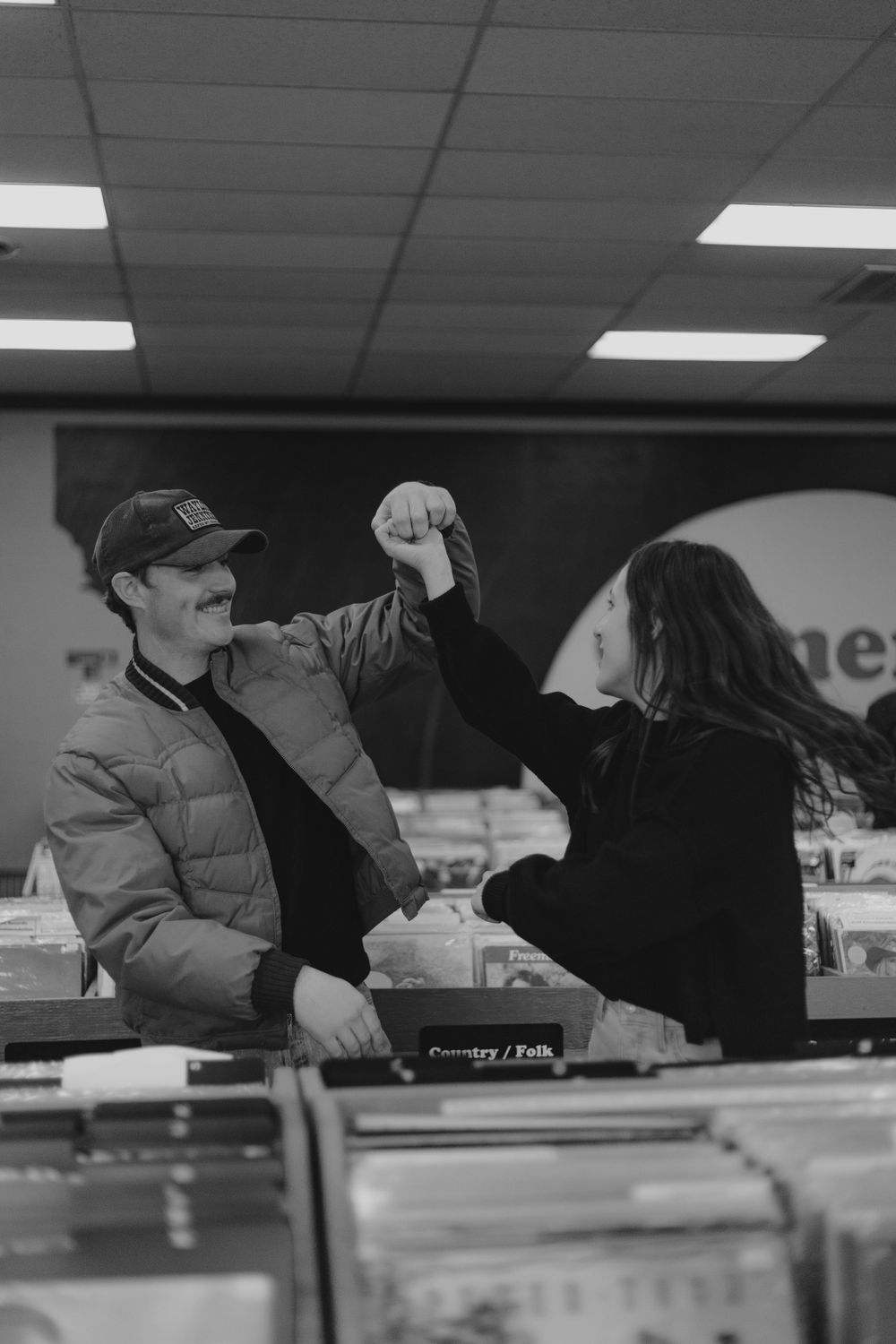 Two people in a record store giving each other a high five over the record bins in a black and white photo.