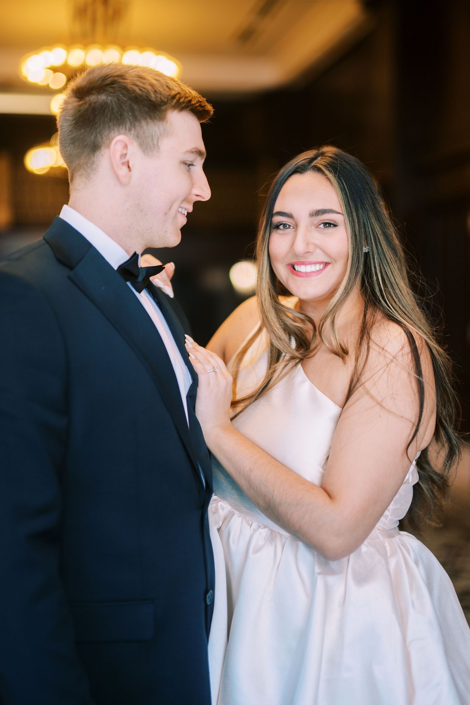 A bride and groom share a joyful moment together at their wedding reception with warm lighting in the background.