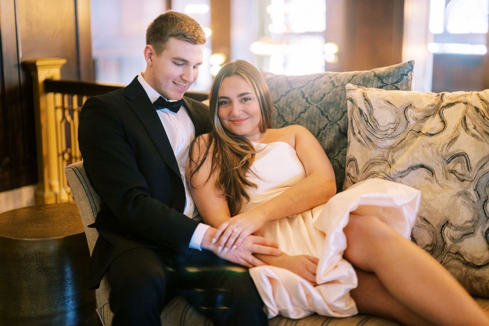 A newlywed couple shares a romantic moment together on an elegant upholstered couch in formal wedding attire.