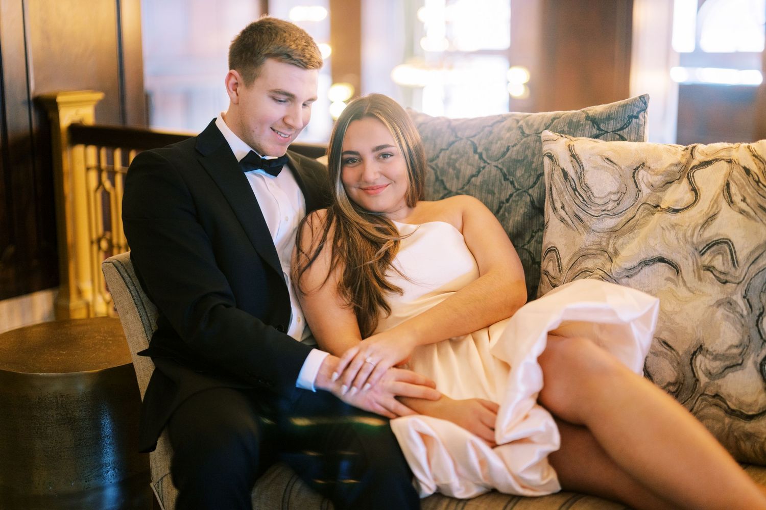 A newlywed couple shares a romantic moment together on an elegant upholstered couch in formal wedding attire.