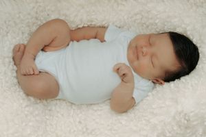 Peaceful sleeping baby in white onesie on plush white carpet.