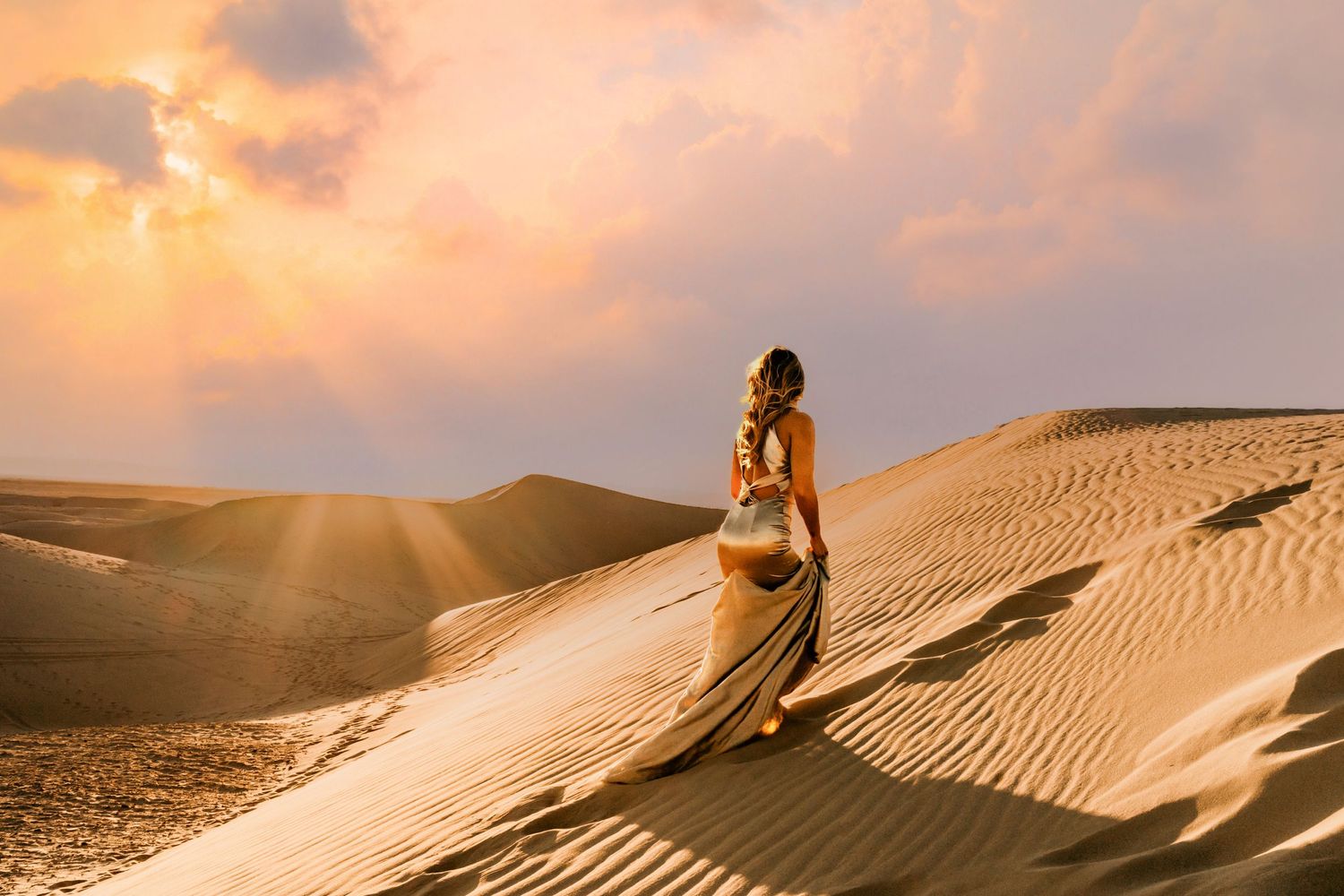 Silhouette on sand dunes at sunset with flowing dress catching golden light.