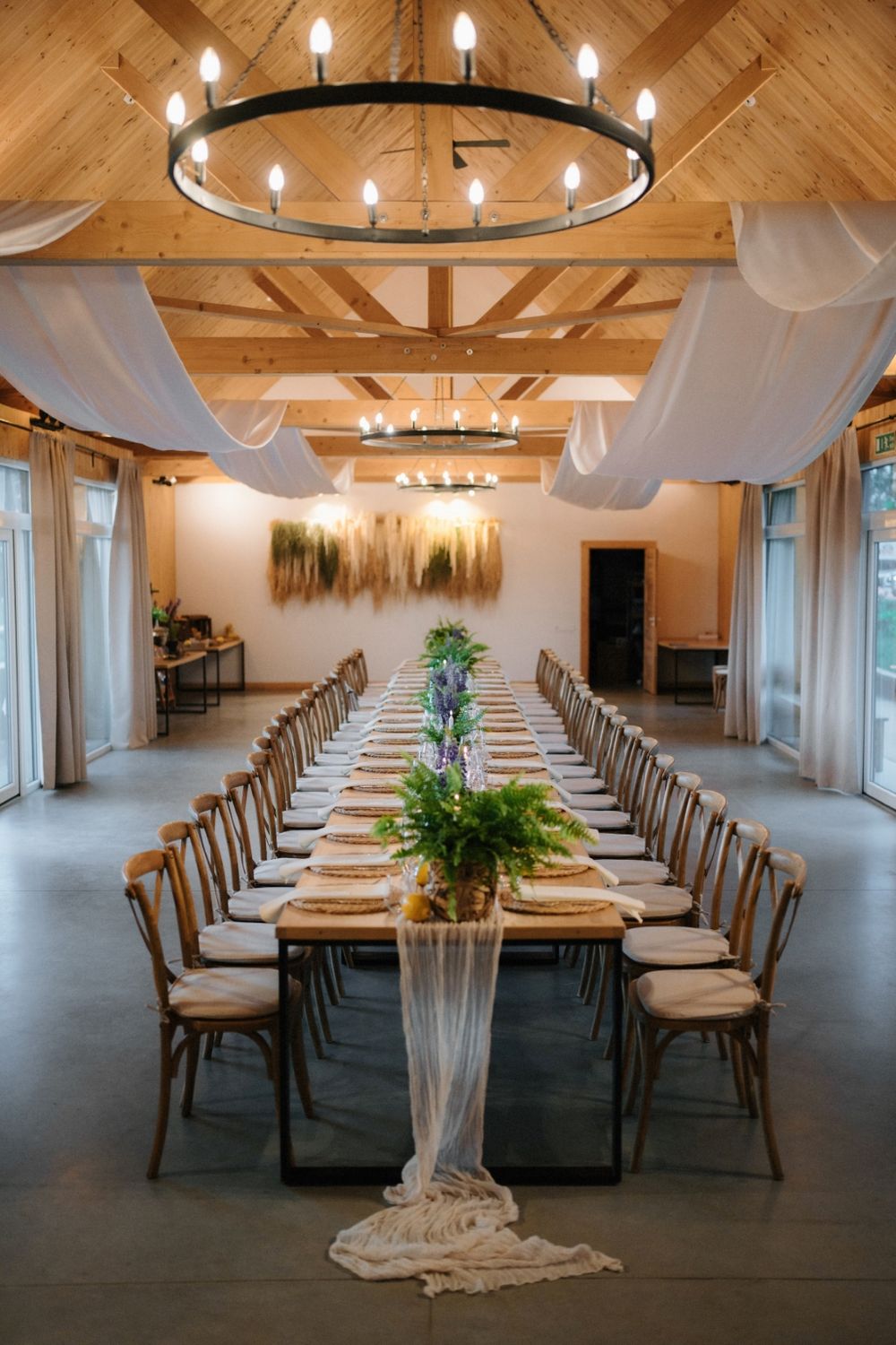 Elegant reception hall with wooden ceiling beams, chandelier lighting and long dining tables.
