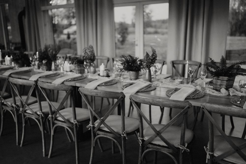 Black and white photo of rustic wedding reception tables with vintage chairs and place settings.