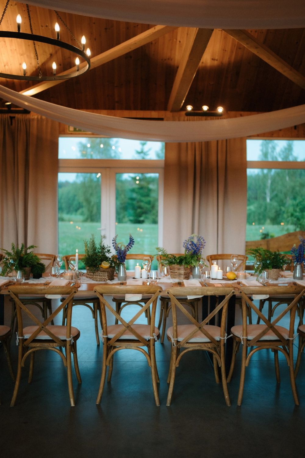 Modern rustic reception venue with wooden crossback chairs and white draping under vaulted ceilings.