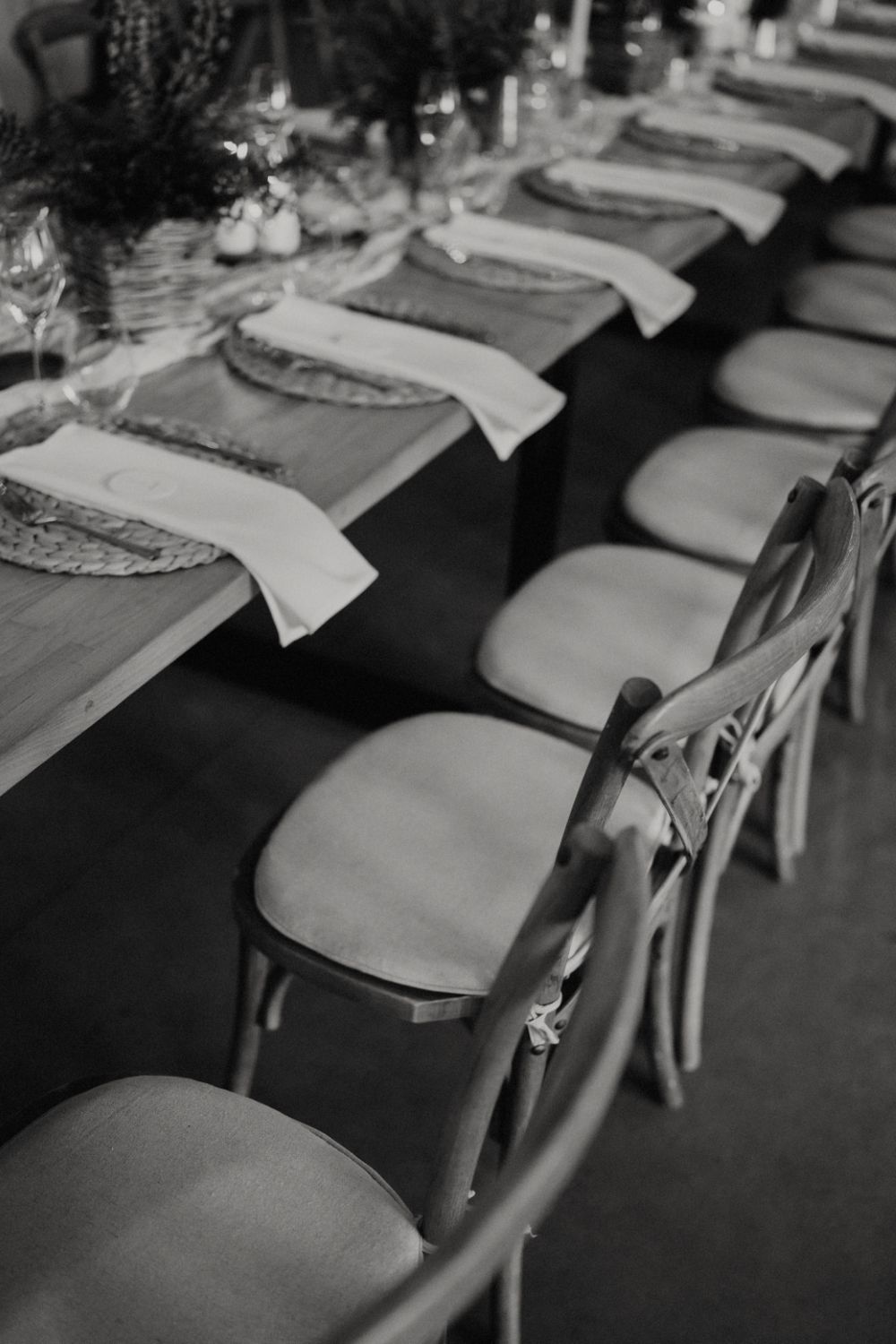 Black and white photo of cross-back chairs lined up at an elegant table setting.