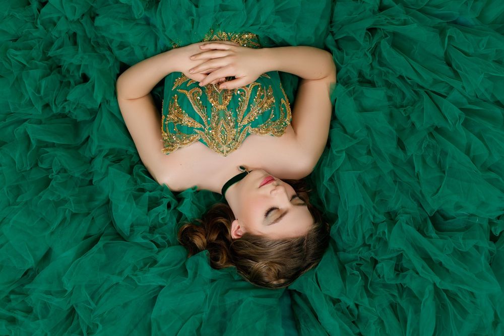 Young woman in a stunning emerald green tulle ball gown lying down, showcasing intricate gold embroidery on the bodice.