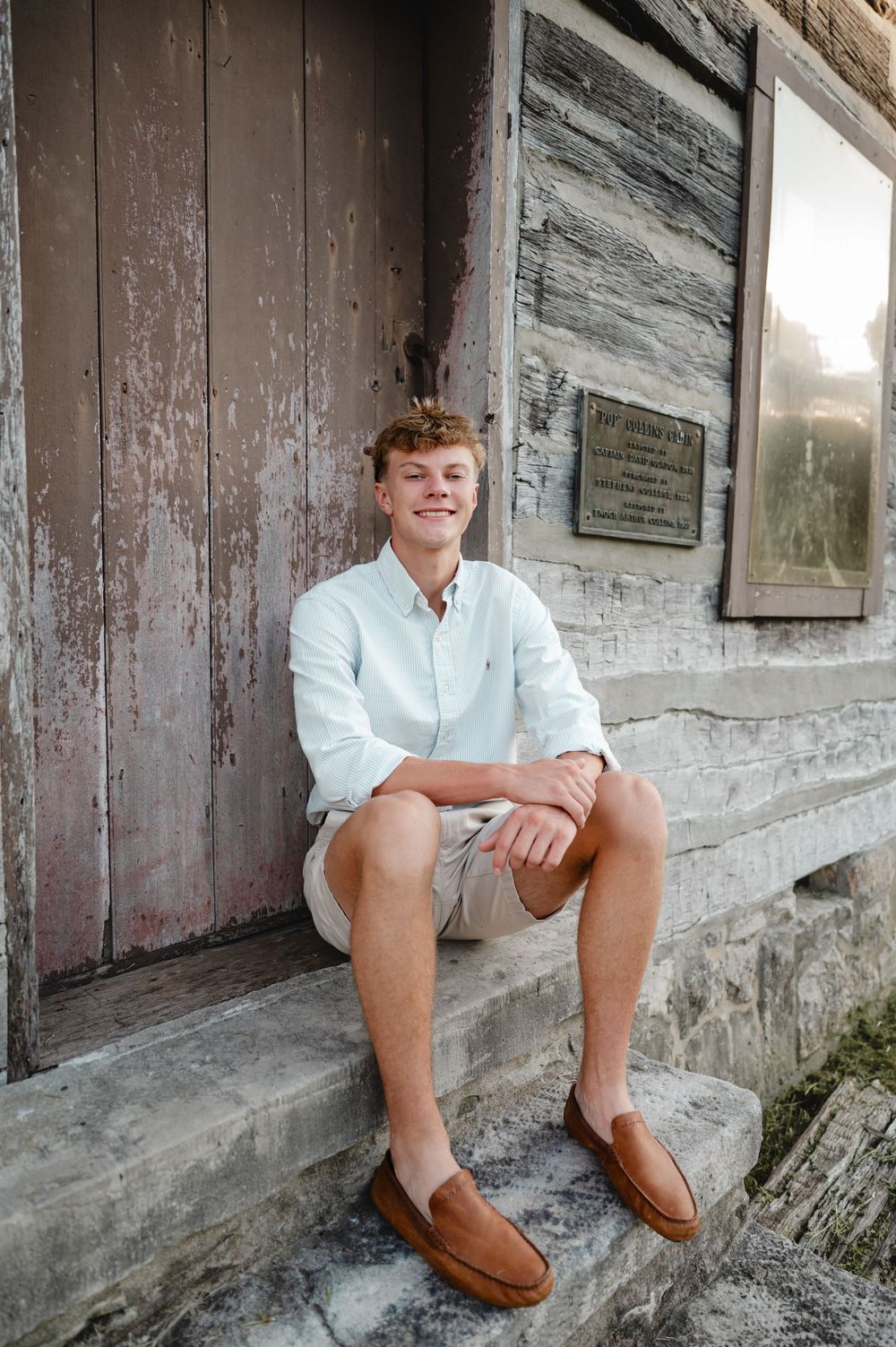 Student in white shirt and brown loafers sits on rustic wooden bench.