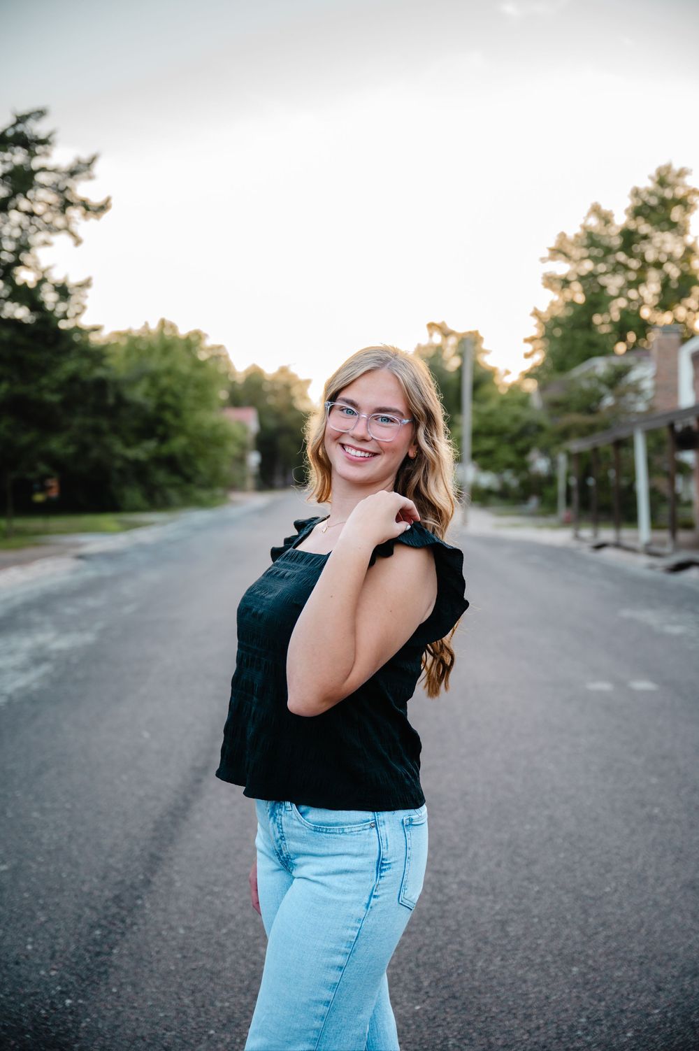 A casual portrait on a quiet suburban street at sunset wearing a black top and light jeans.