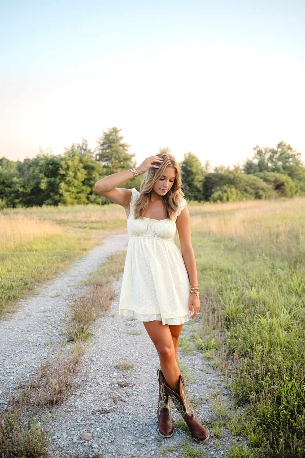 Woman in white dress twirls on gravel path surrounded by wildflowers and summer greenery.