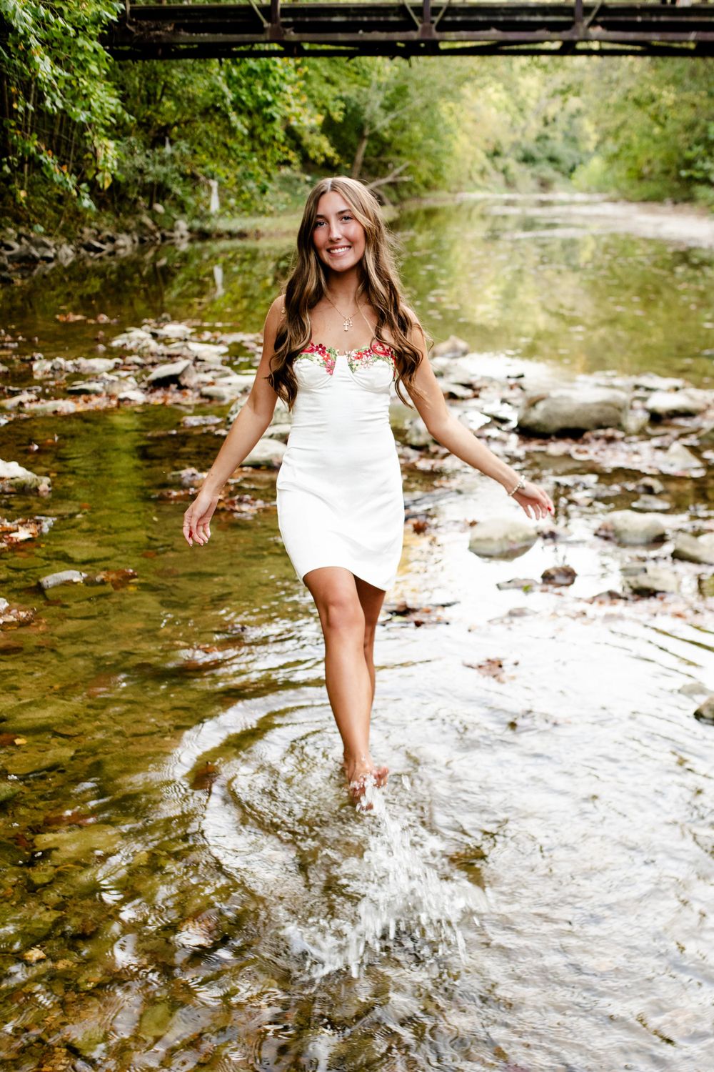 Senior photo of a client playfully kicking water in a pond during a summer session, capturing fun and carefree moments.