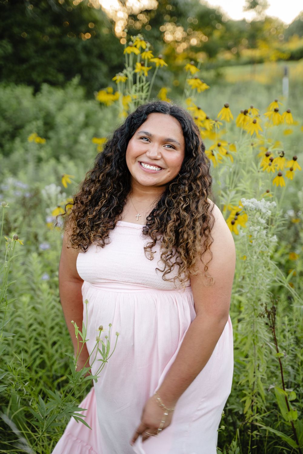 Woman in pink dress smiles while posing among yellow wildflowers at sunset.