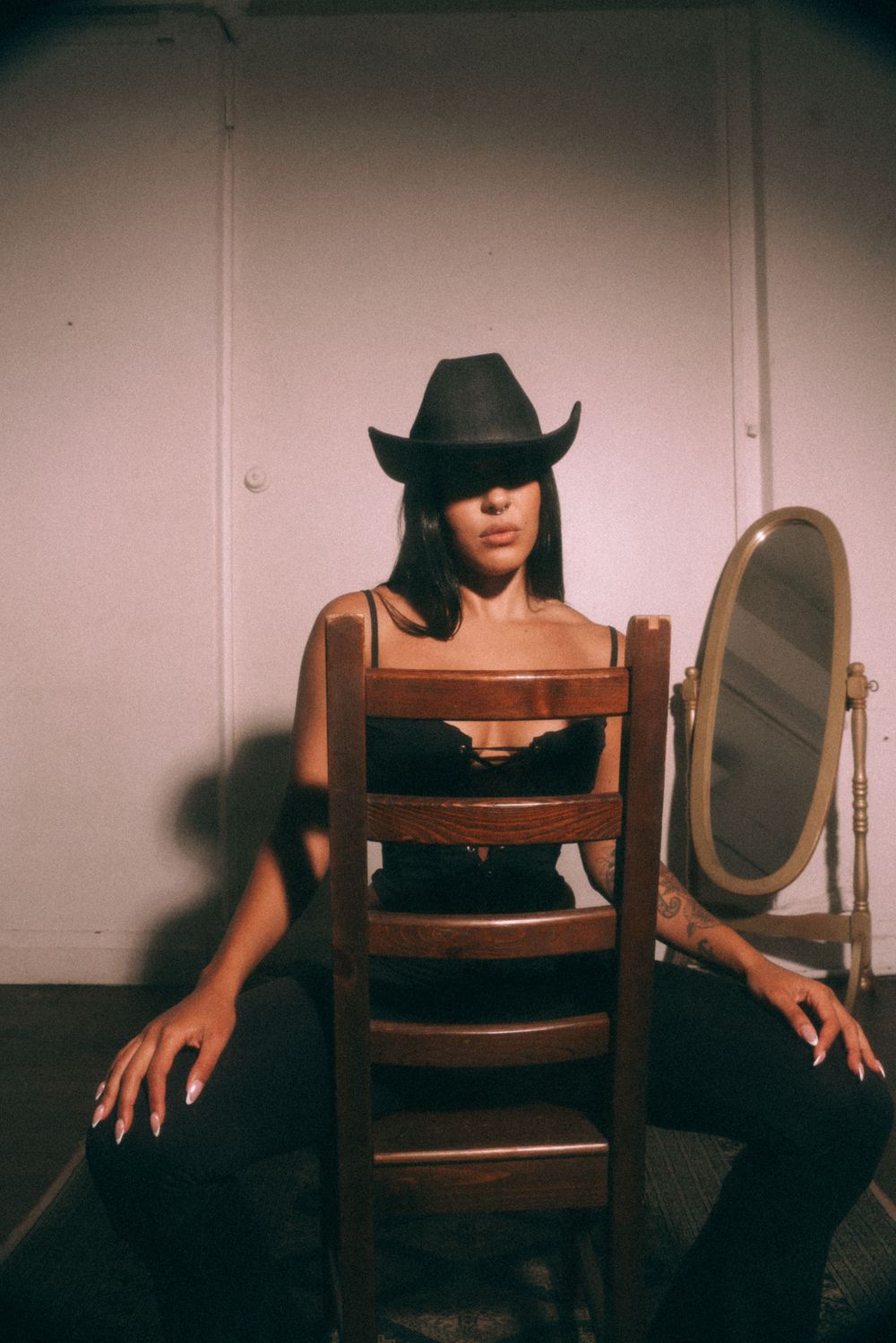 Artistic portrait with cowboy hat sitting backwards on wooden chair with mirror.