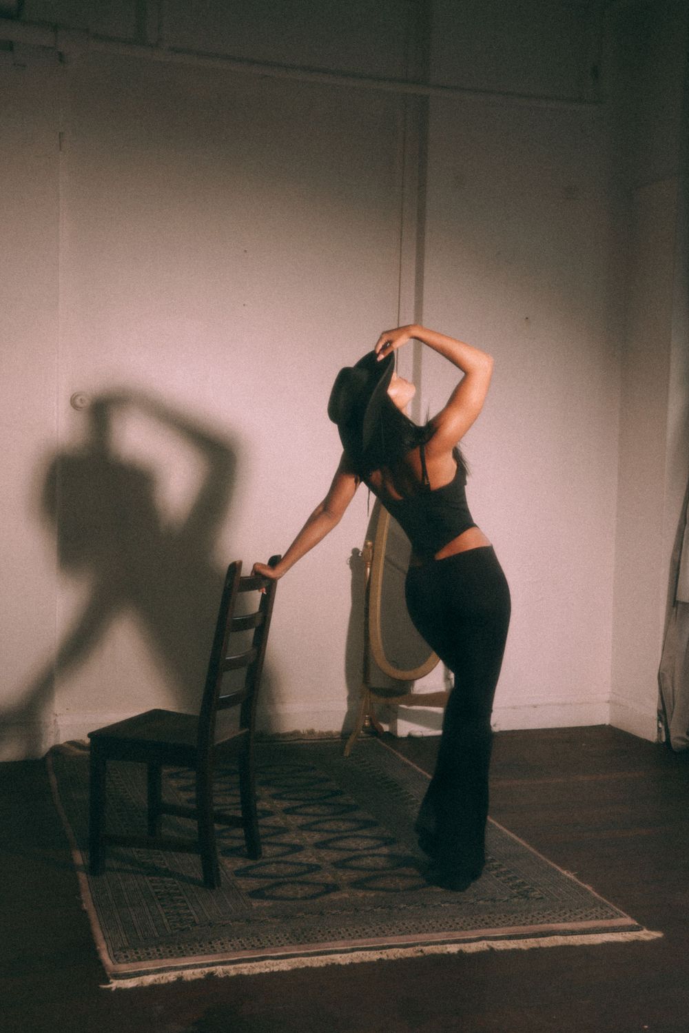 Silhouetted dance pose with chair and mirror in dimly lit studio setting.