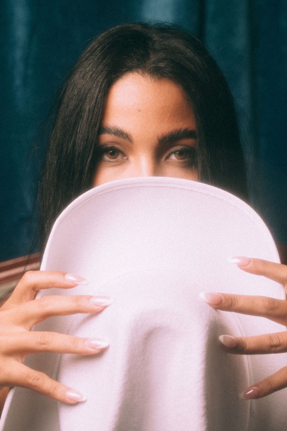 Artistic beauty shot with white circular prop covering lower face against dark background.