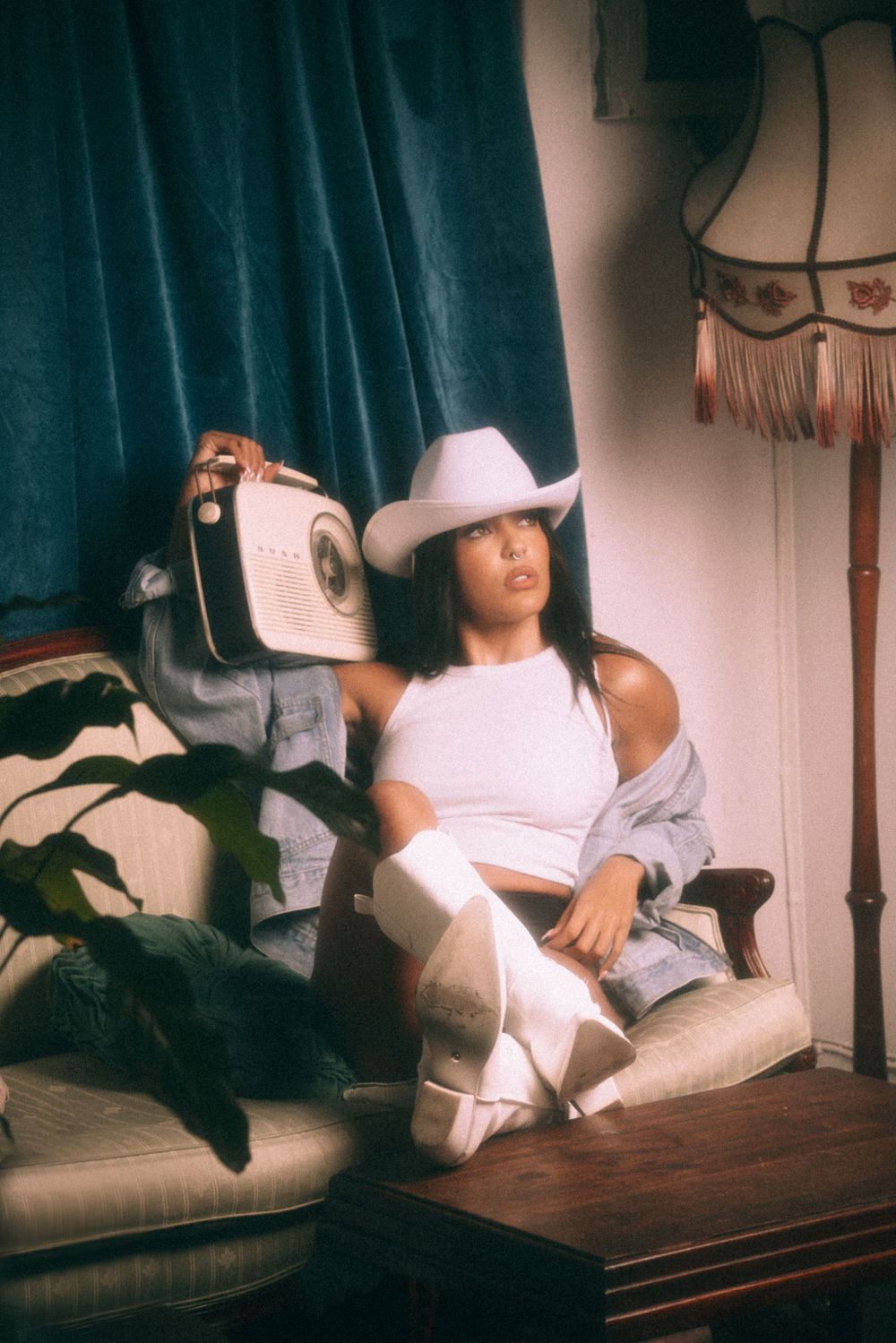 Casual portrait in white tank top and cowboy hat sitting on vintage couch.