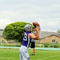 Football player in purple jersey catching a ball during an outdoor practice on a green field.