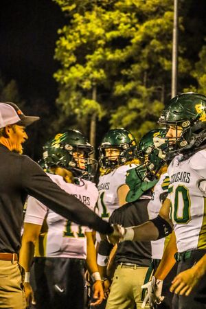 Football coach shaking hands with green and white uniformed Cougars players during a night game.