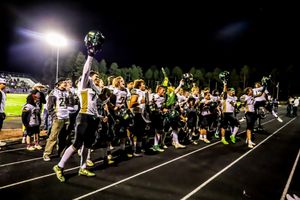 Victorious green and black football team celebrating on the track after a night game win.