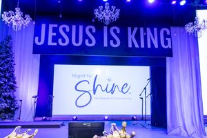 Night to Shine Tim Tebow Foundation event stage with Jesus Is King banner and chandelier decor.