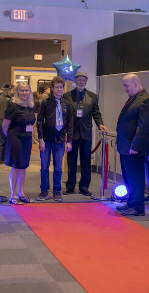 Four people standing on a red carpet at a formal event near a velvet rope entrance.