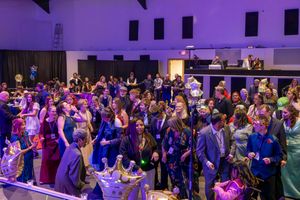 Large crowd of dressed-up guests celebrate at Night to Shine prom event under purple lights.