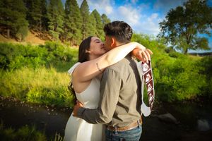 Happy couple sharing a romantic kiss outdoors near a river surrounded by lush green trees.