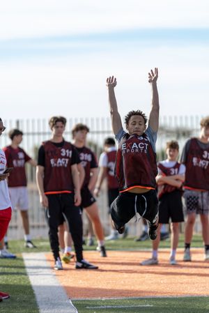 Young athlete performs long jump at Exact Sports combine event with teammates watching in background.
