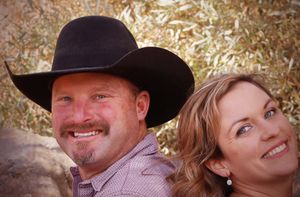 A smiling couple outdoors, man wearing a black cowboy hat, woman with pearl earrings.