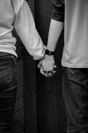 Black and white close-up of couple holding hands, woman with dark nail polish and smartwatch.
