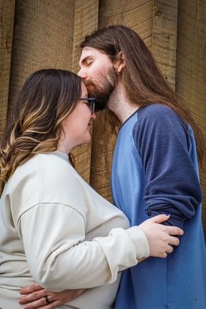 Romantic couple sharing a kiss against rustic wooden barn wall, woman in white sweatshirt.