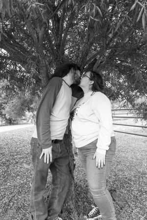 Couple kissing under a large tree in black and white outdoor portrait photography.
