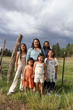 Native American mother posing with four daughters near wooden fence post under stormy sky.