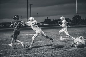 Black and white action shot of football players during a night game on the field.